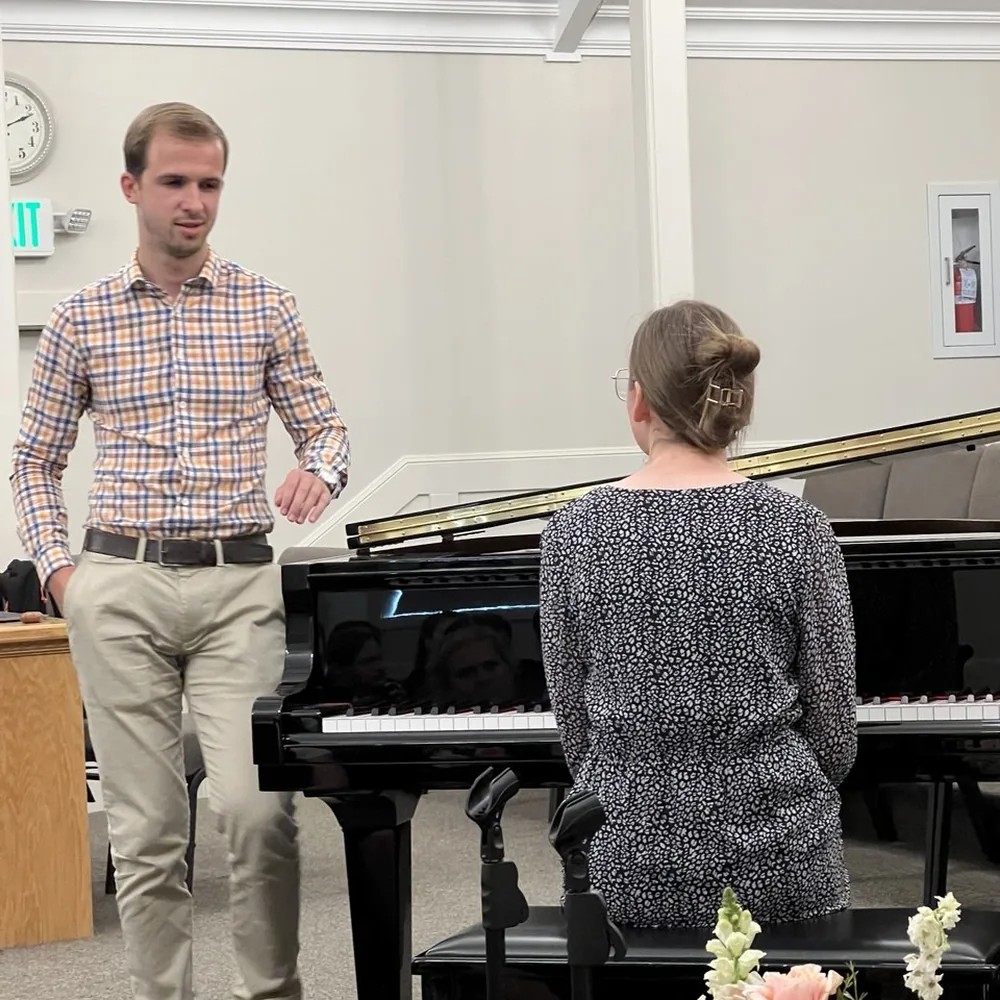 A student playing a grand piano in a hall during a lesson