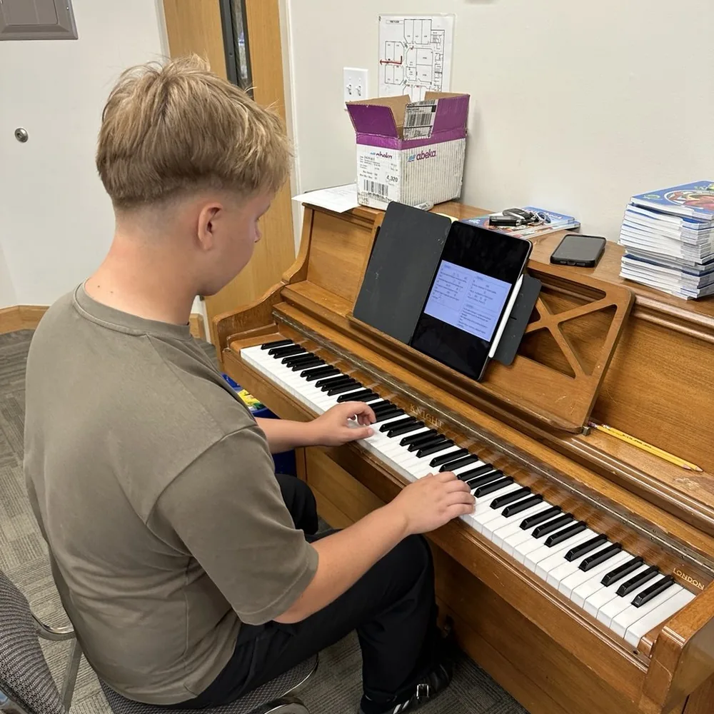 A teenager playing an upright piano during an online lesson